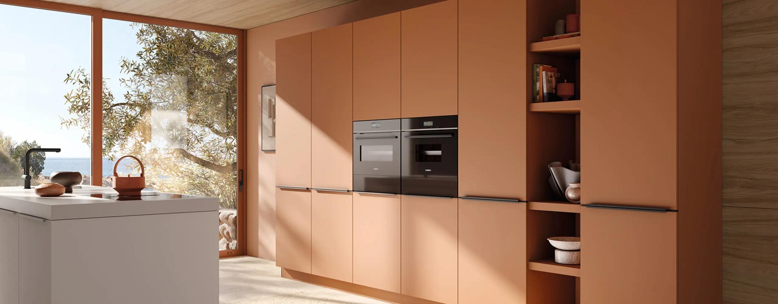 Moderne Küche in Terrakotta mit eleganten Einbauschränken und Geräten in Schwarz. Große Fenster mit Meerblick und hellem Tageslicht verleihen der Küche eine warme, mediterrane Atmosphäre.